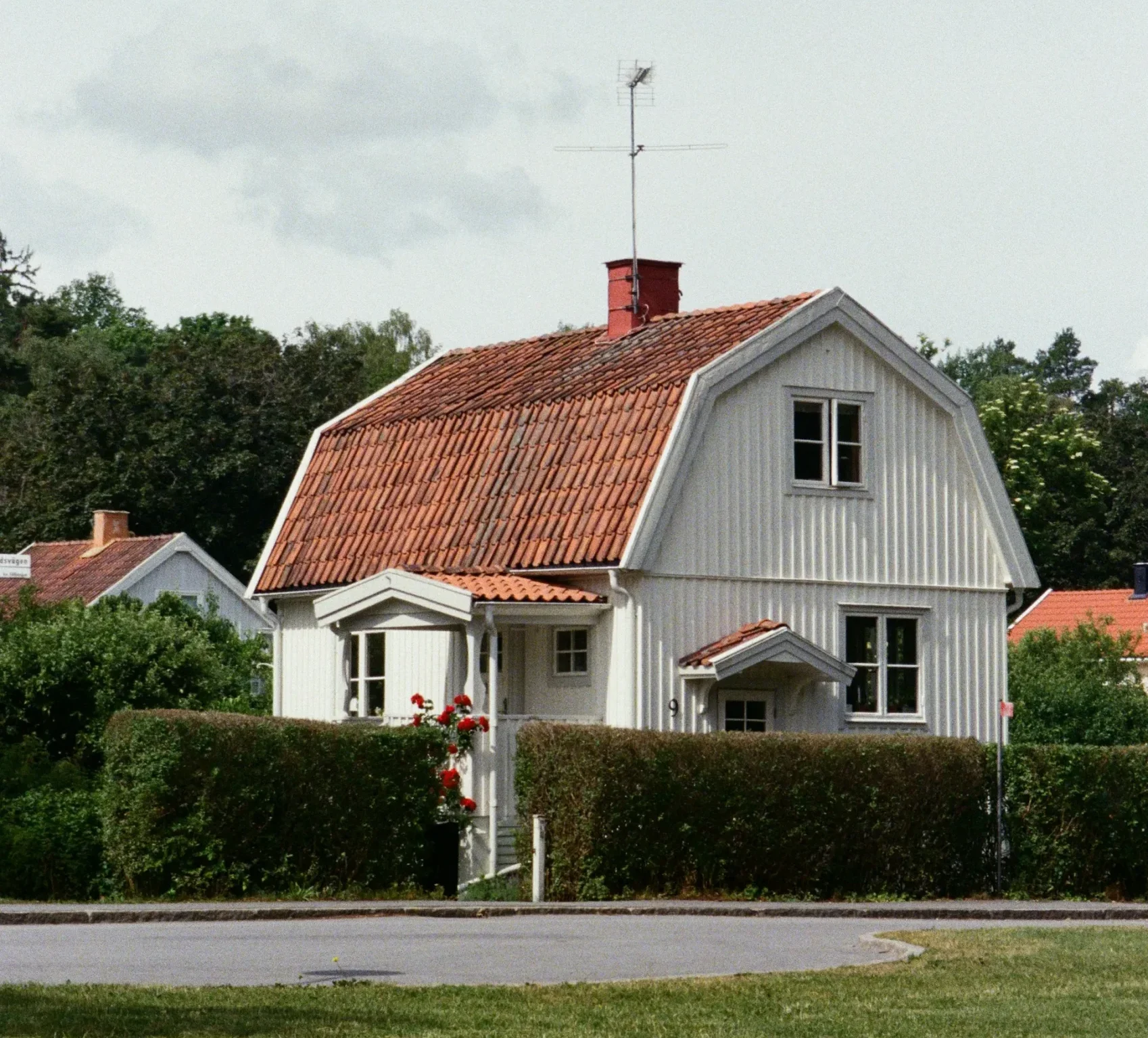 Vitt hus med rött, kurvat tak och häck runt tomten